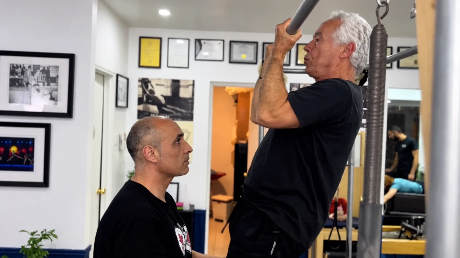 Alumno trabajando fuerza en Cadillac con el acompañamiento de su instructor en Posición Pilates